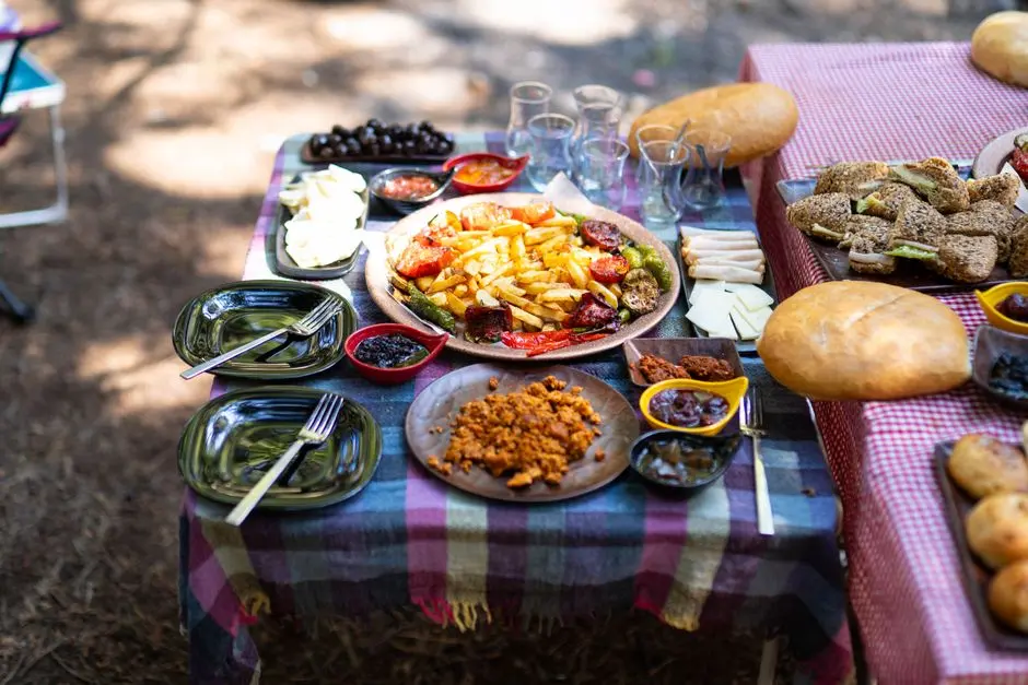 A vibrant outdoor picnic setup with various fresh dishes, bread, and tableware on a checkered cloth.