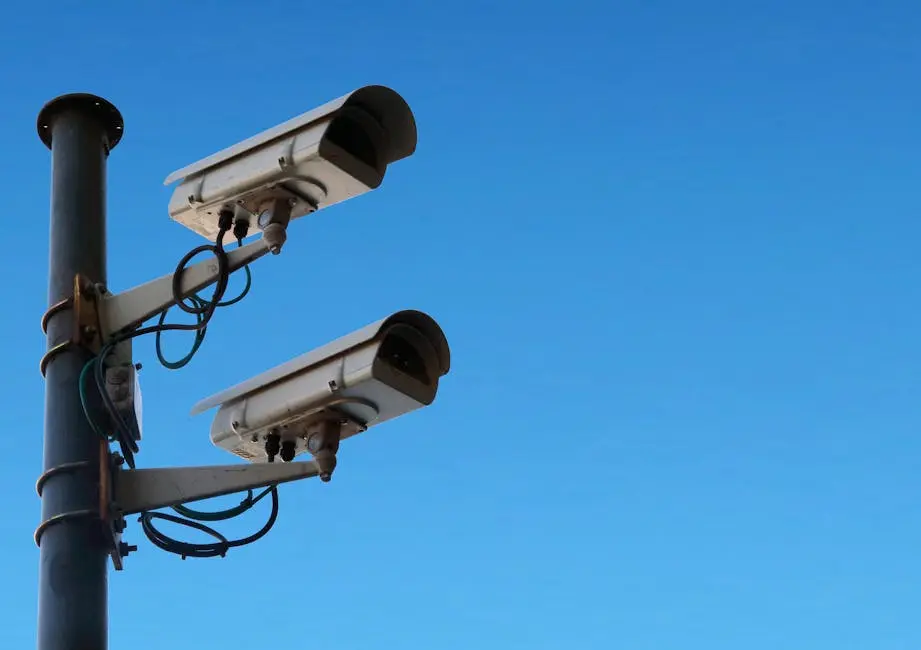 Two security cameras mounted on a pole with a bright blue sky as the backdrop.