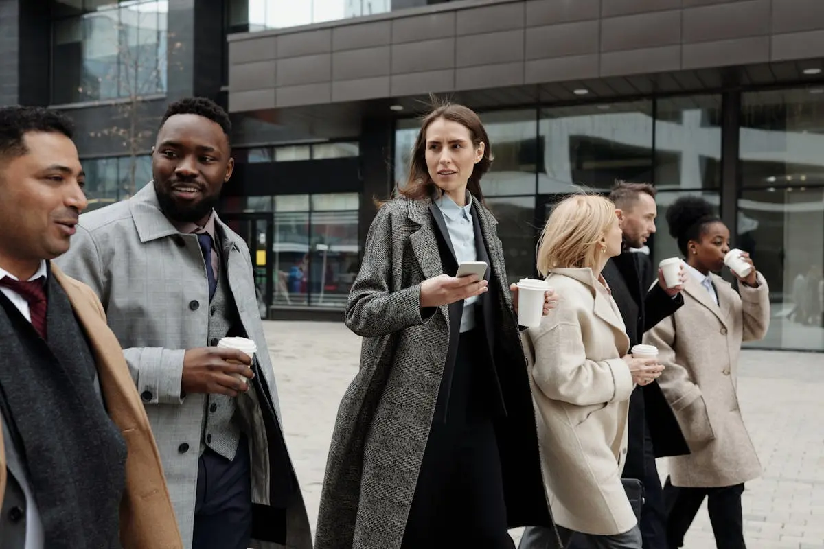 A diverse group of business professionals walking outside a modern building, enjoying coffee and conversation.