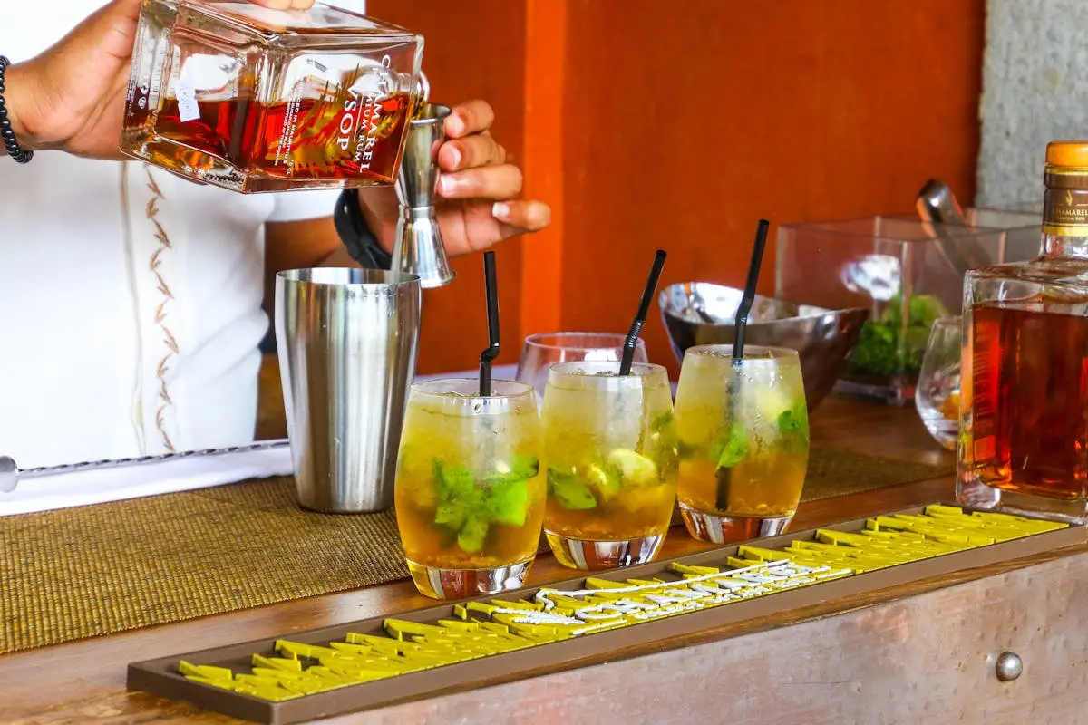 Bartender pouring rum into cocktail glasses at a vibrant bar setting.