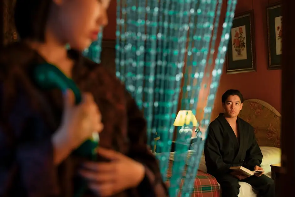 A couple in robes enjoys a quiet moment in a warmly lit bedroom with a beaded curtain.