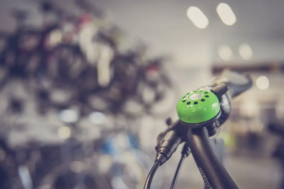 Close-up of a green bicycle bell on handlebars with blurred bike shop in background.