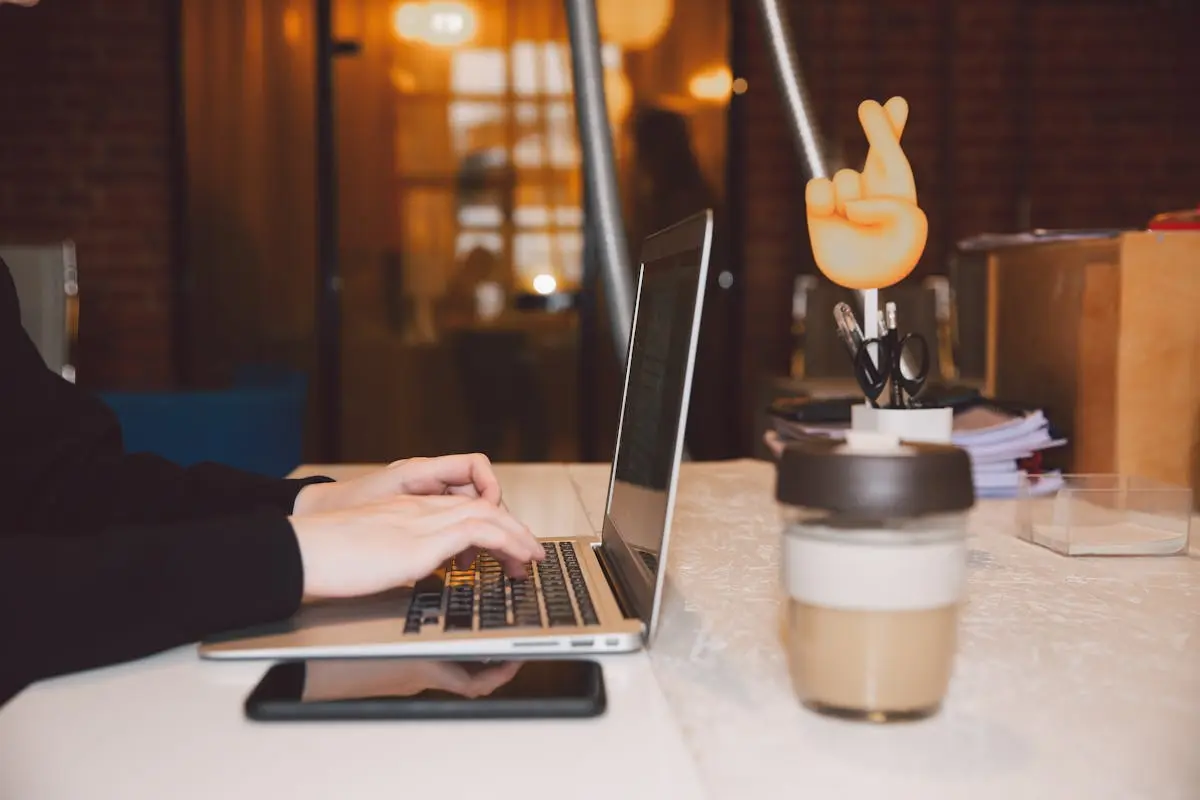 Close-up of hands typing on a laptop in a modern office setting with coffee and creative decor. Virtual CFO