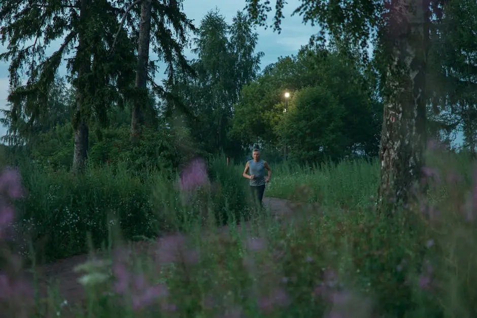 A man jogging along a forest pathway at twilight surrounded by lush greenery.