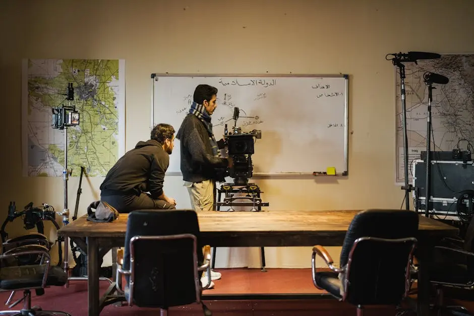 Two men setting up a camera in an indoor film studio. Maps and equipment surround them.