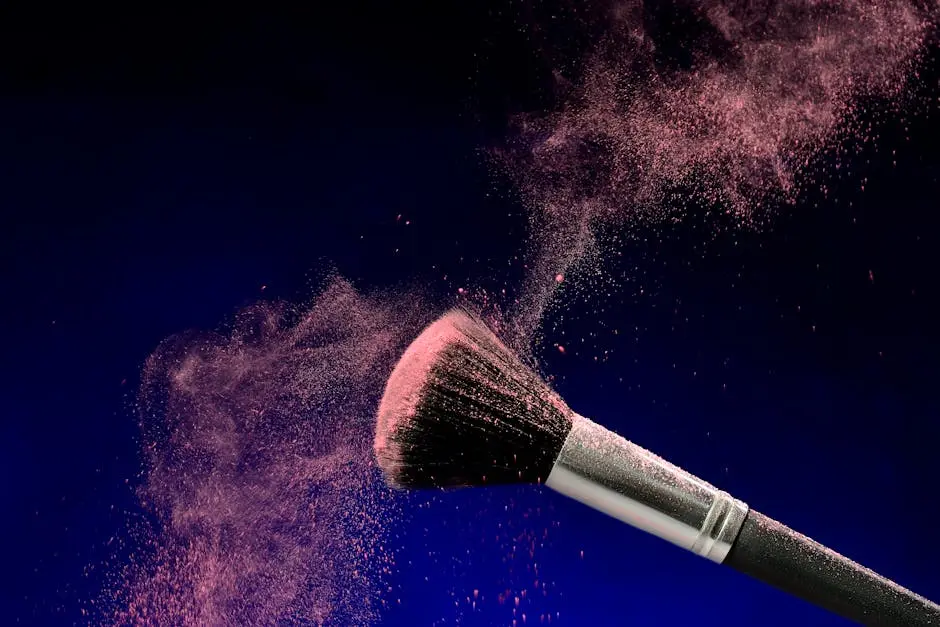 Pink powder swirls around a makeup brush against a dark background, showcasing elegance and beauty.