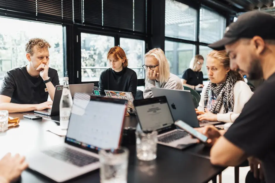 A group of professionals engaged in digital work on laptops and smartphones in a modern office environment.