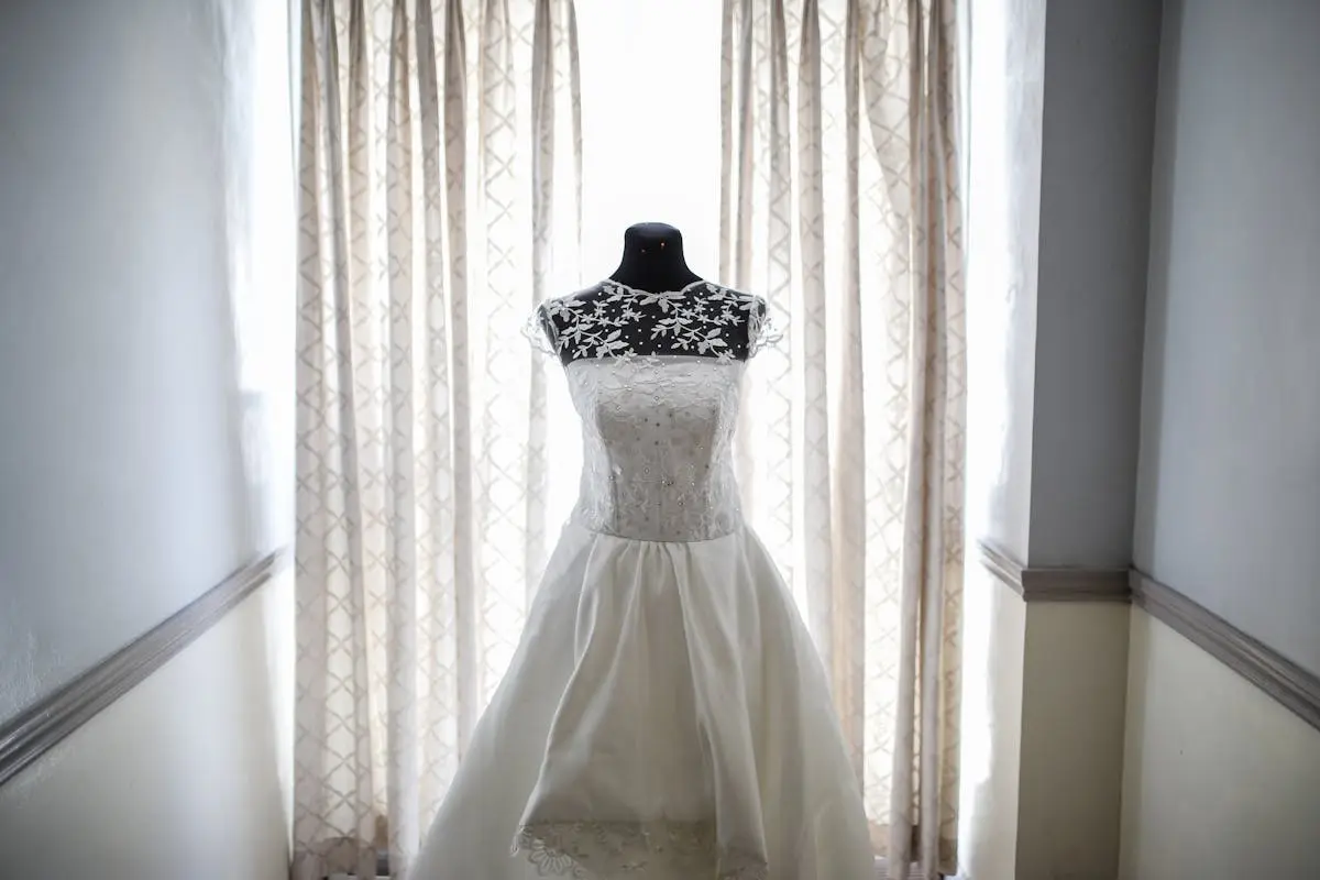 A beautiful bridal gown displayed on a mannequin, illuminated by natural light from a window.