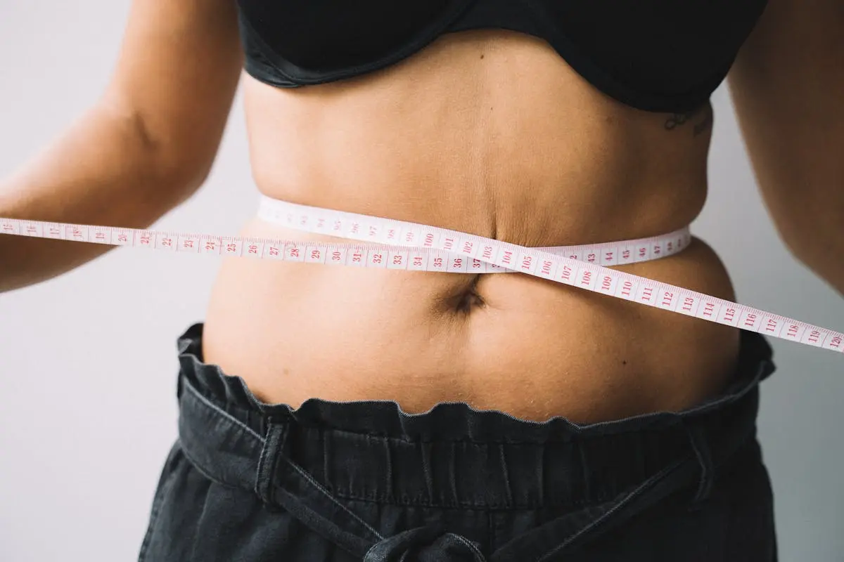 A person measuring their waist with a tape, symbolizing fitness and health goals.