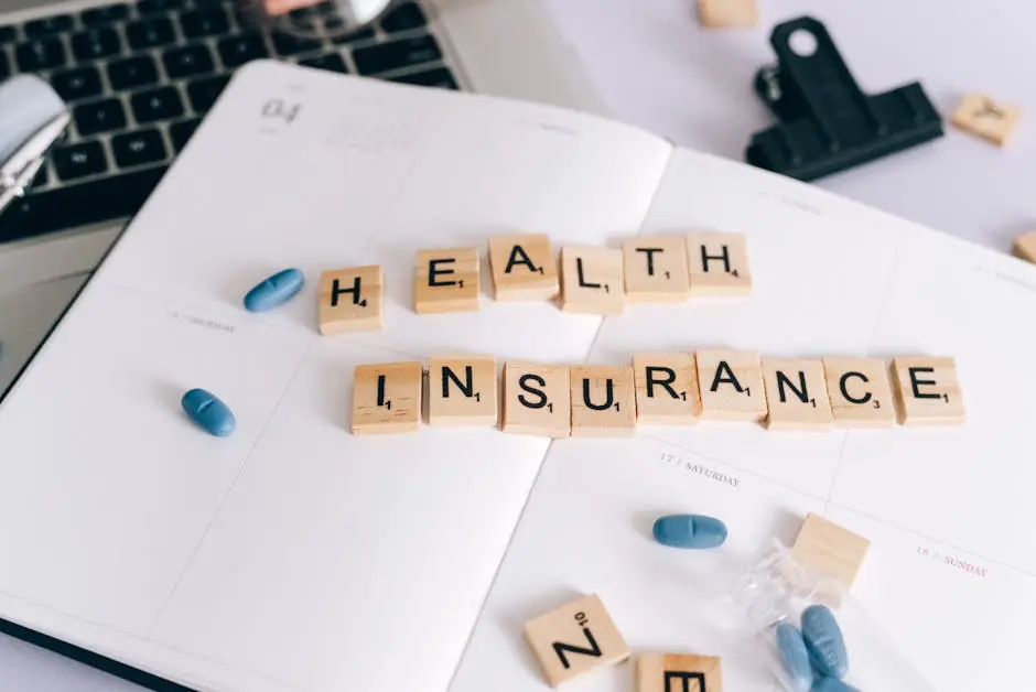 Scrabble tiles spelling ‘Health Insurance’ on planner with pills and laptop, symbolizing healthcare planning.