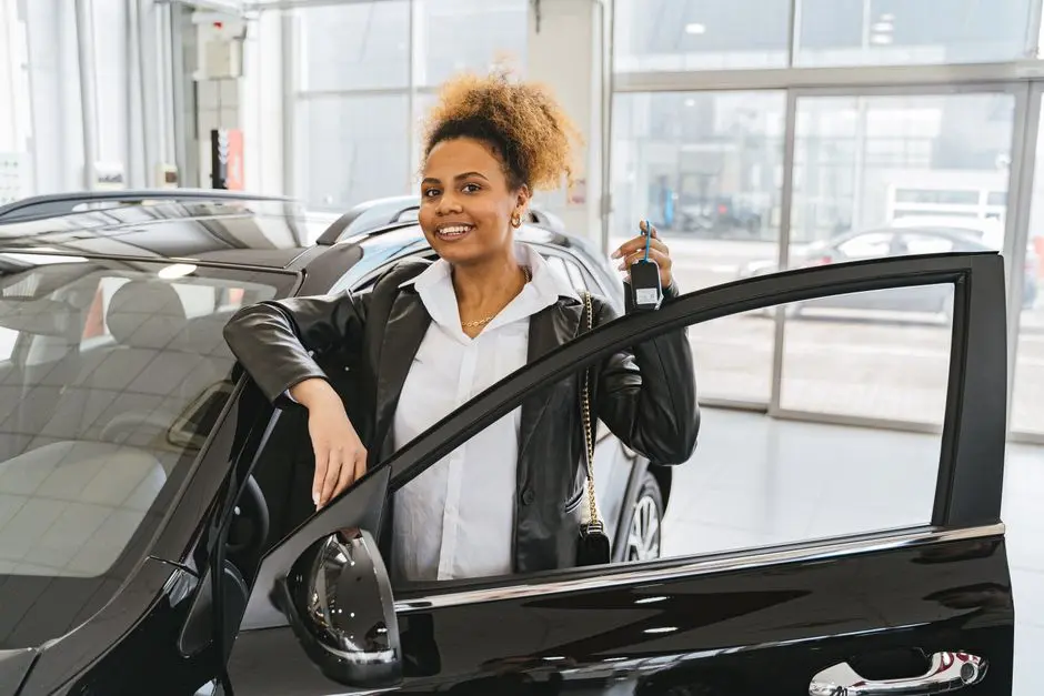 Smiling woman holding car key in dealership showroom next to new vehicle.