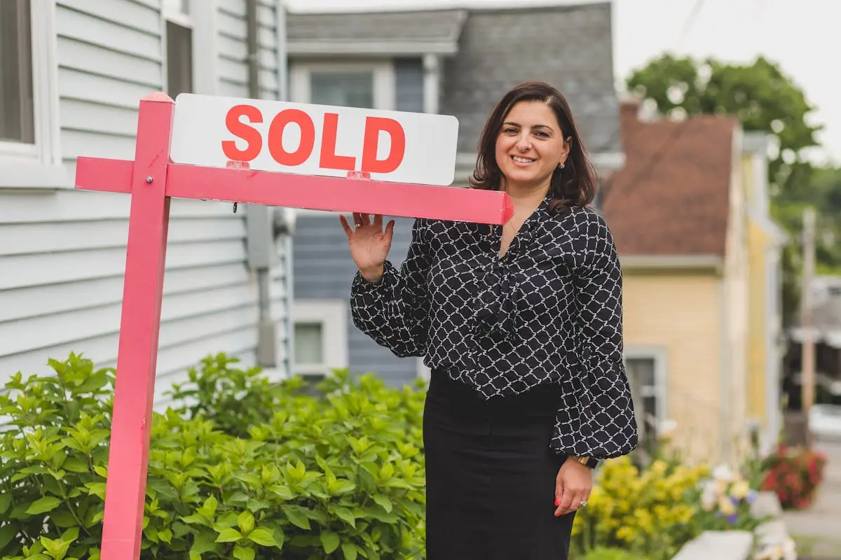 Smiling real estate agent standing outdoors with a sold sign, symbolizing success and achievement in property sales.