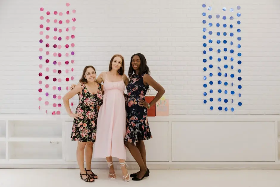 Three women in stylish dresses pose joyfully indoors against a decorative backdrop.