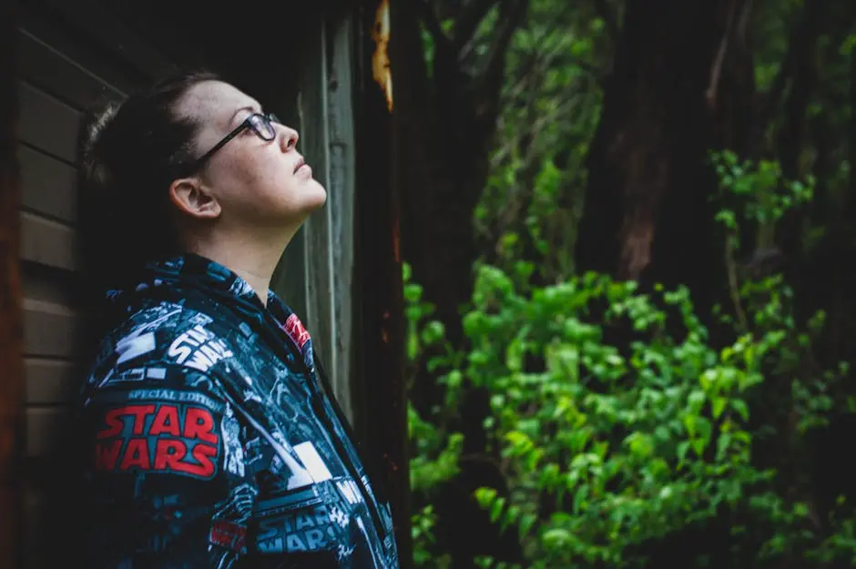Profile of a woman standing outdoors, wearing a Star Wars jacket, surrounded by greenery.