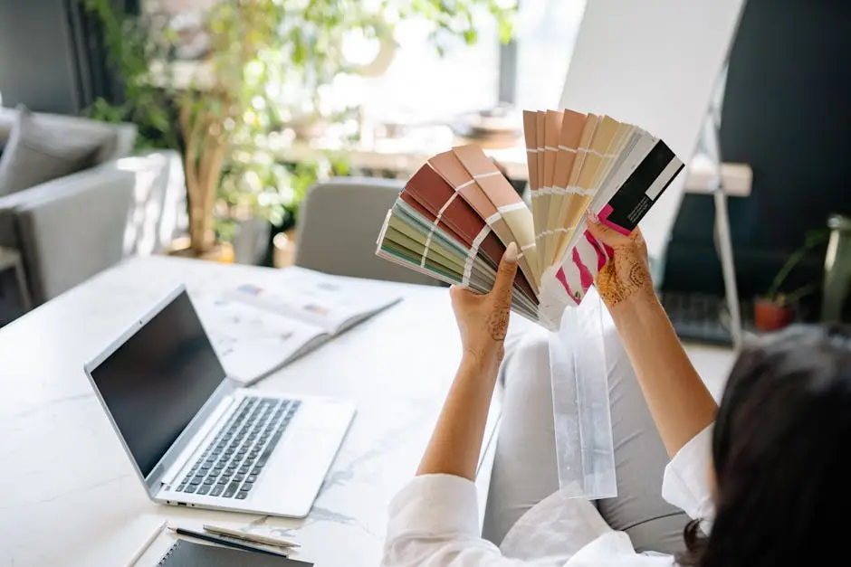 Interior designer analyzing color swatches with a laptop and plants in a bright office space.