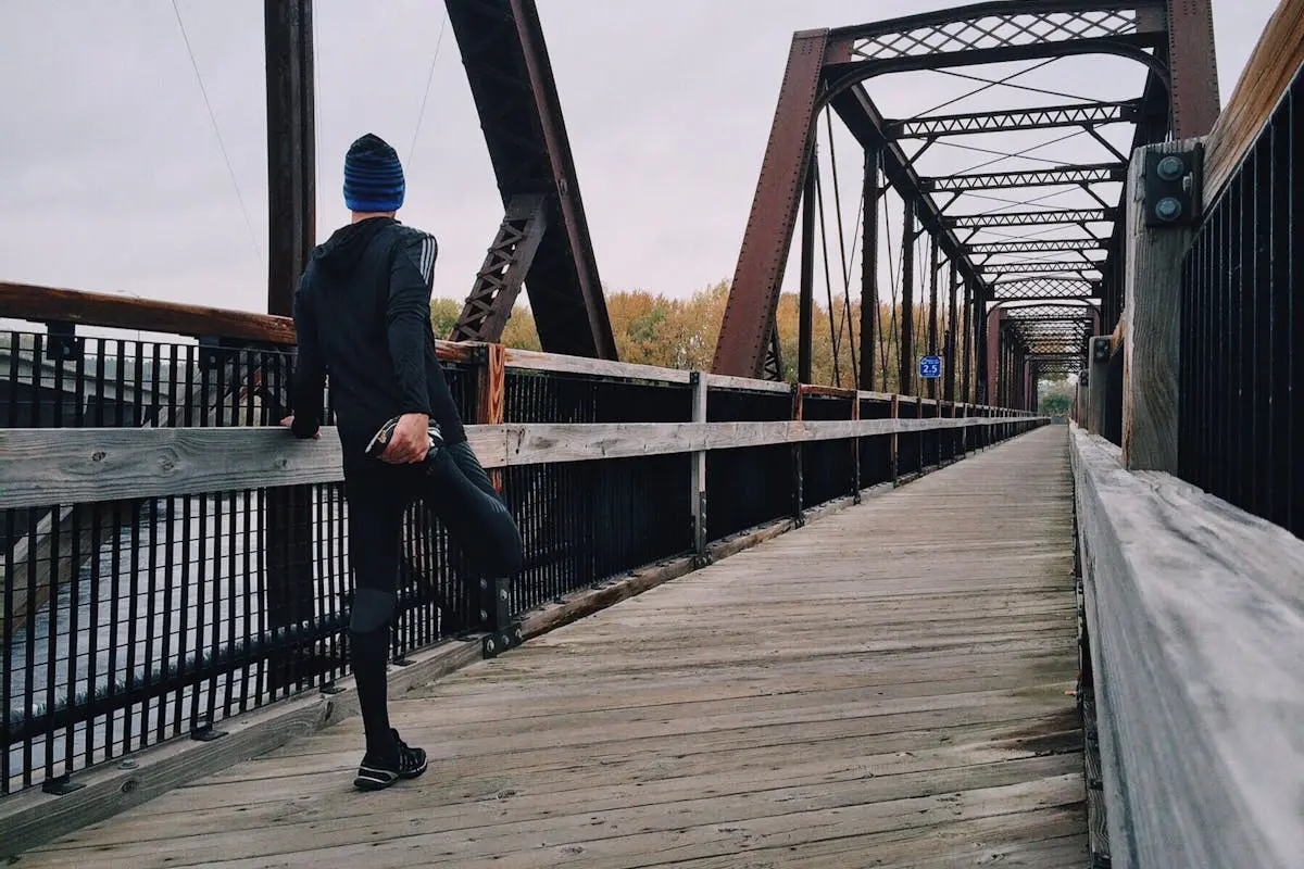 Man stretching on a wooden footbridge during a daytime run on an iron bridge, emphasizing fitness and recreation.