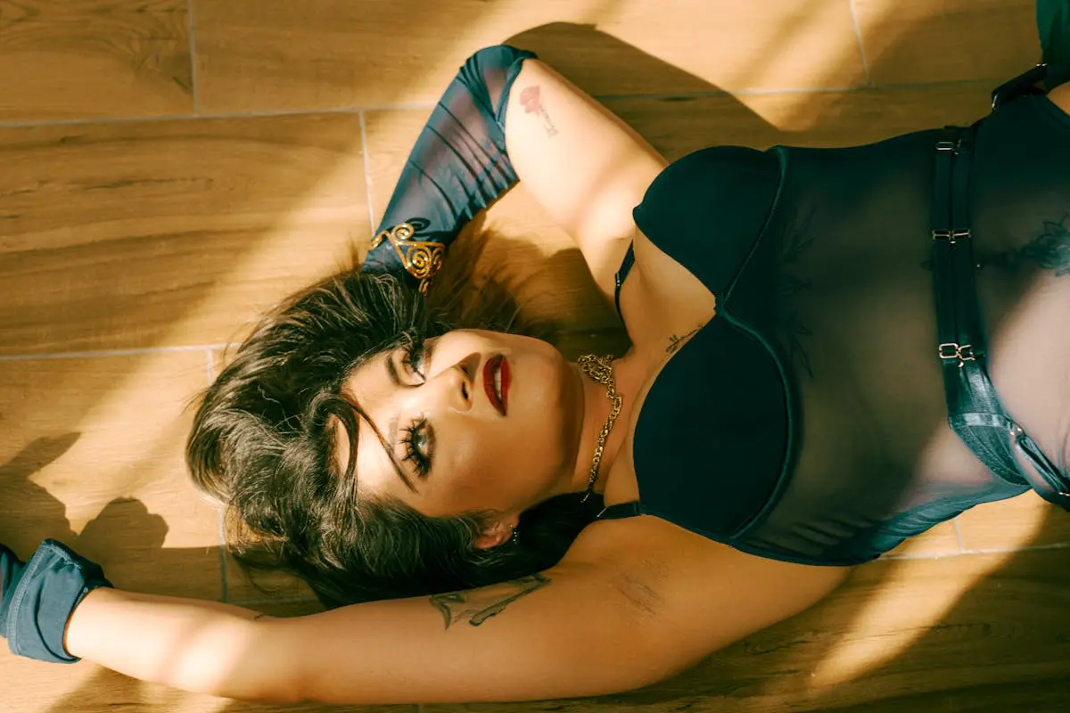 Elegant lingerie fashion shoot with woman posing on wooden floor in dramatic lighting.