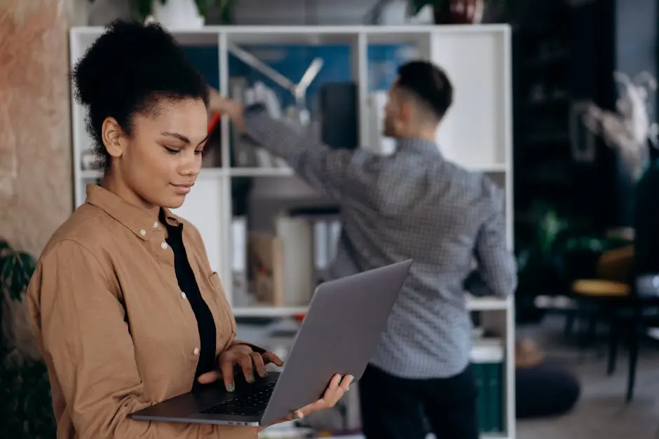 Confident young businesswoman working on a laptop in a modern office setting.