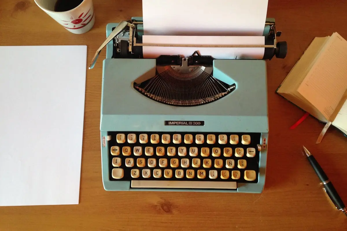 Classic blue typewriter on a wooden desk with paper, pen, and notepad, evoking vintage nostalgia.