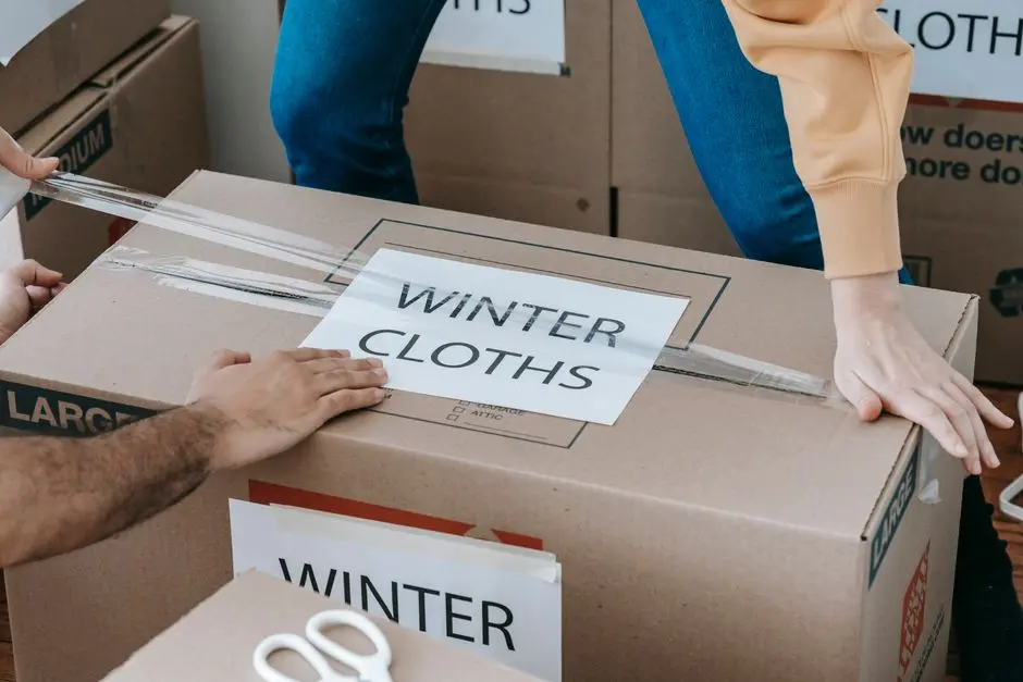 Close-up of hands packing a box labeled ‘Winter Clothes’ for relocation, emphasizing organized moving.