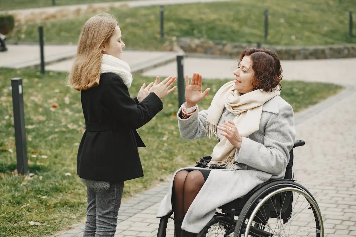 A girl and a woman in a wheelchair enjoying playful bonding in a park setting.