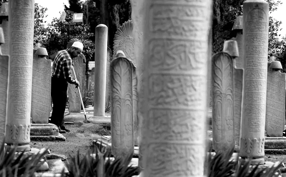 A man raking the ground among historic stone graves, creating a serene and respectful atmosphere.