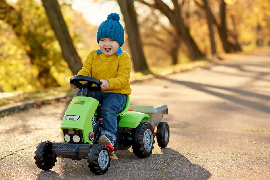 A playful young boy rides a green toy tractor on a sunny autumn day.