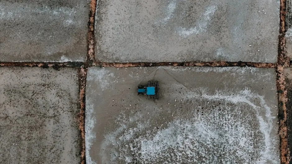 Drone shot of a blue tractor on geometric salt flats, showcasing farming in a unique landscape.