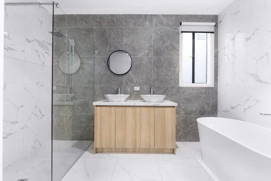 A sleek and stylish modern bathroom with minimalist design, featuring dual washbasins, marble tiles, and a glass shower enclosure.