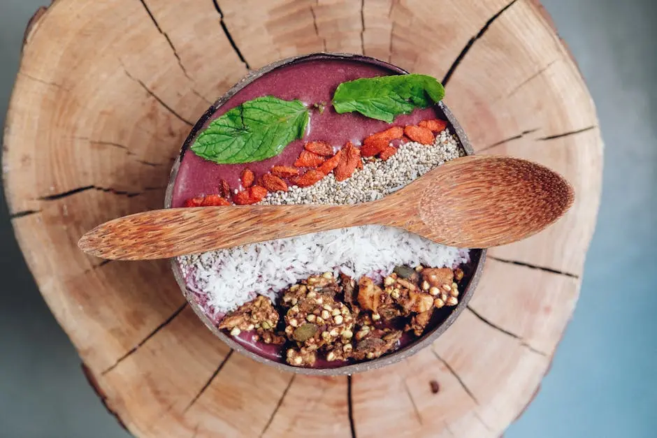 Healthy acai bowl with granola, mint leaves, and berries served on rustic wood.