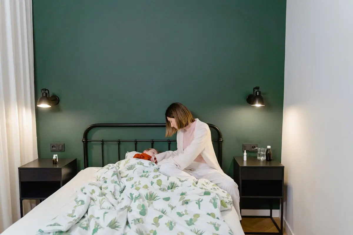 A mother cares for her child with a fever in a warm, cozy bedroom setting.
