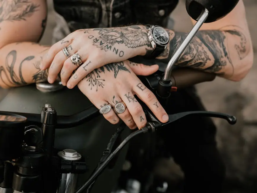 Close-up of tattooed hands with rings on a motorcycle, stylish watch visible.