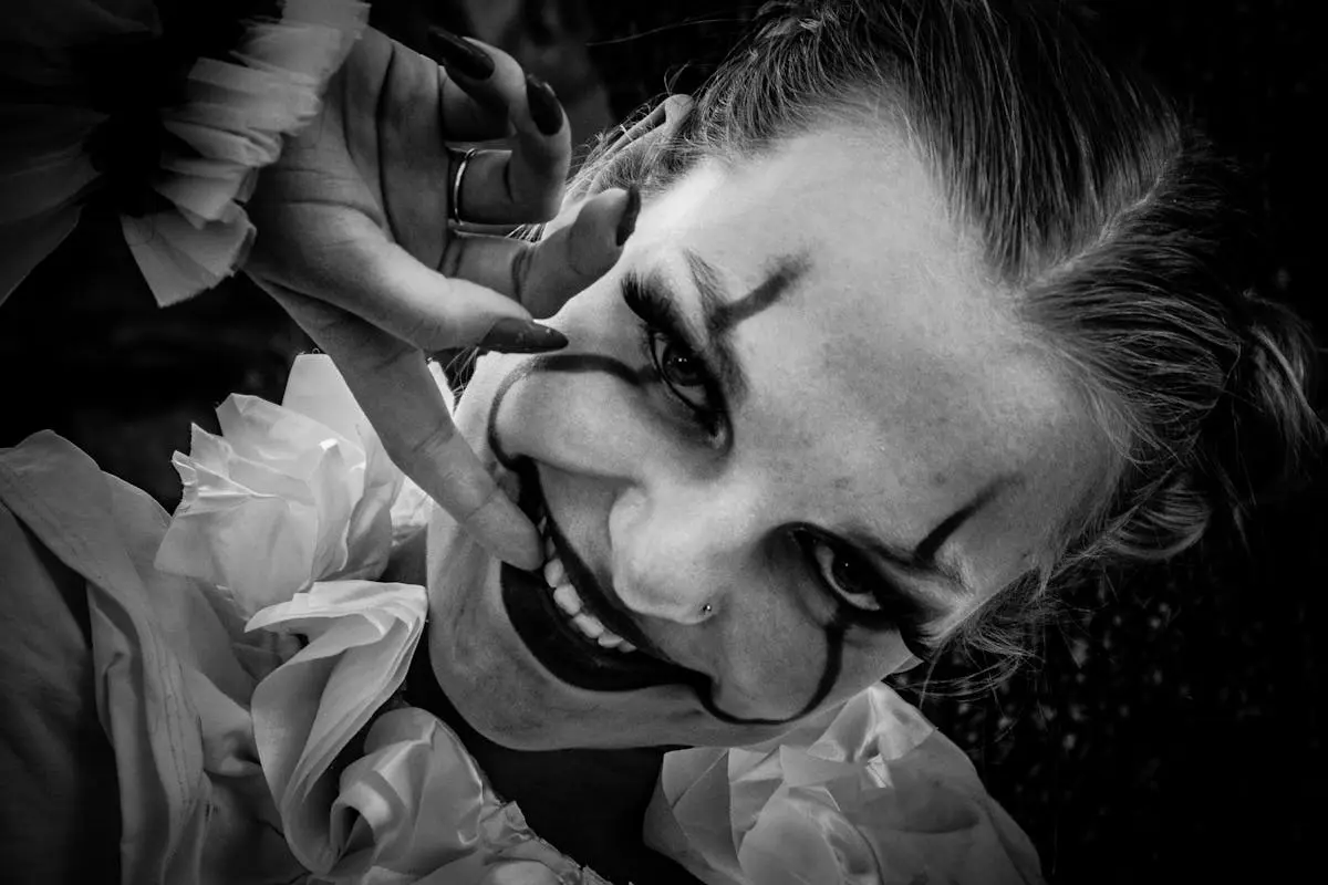 Artistic black and white portrait of a smiling clown woman with makeup, captured in a dramatic angle.