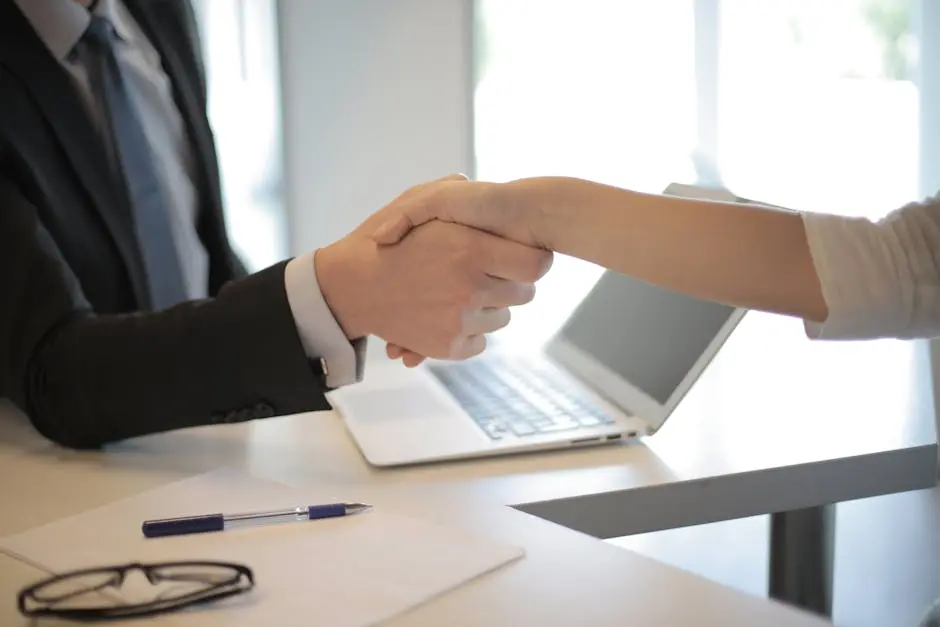 Close-up of a professional handshake over a laptop during a business meeting in an office. Outsourced CFO Services