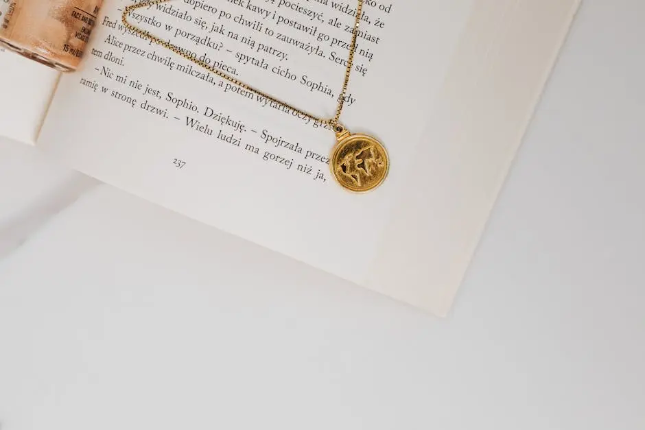 A close-up view of a gold pendant necklace resting on an open book with white pages and text.