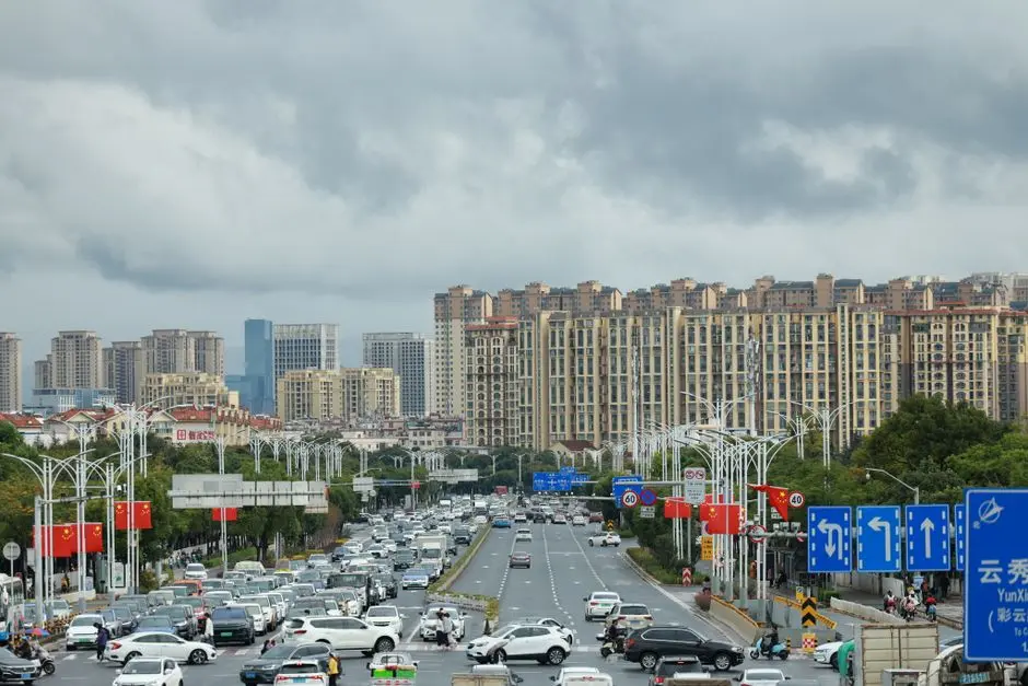 View of heavy traffic on a major road in a modern Chinese city with high-rise buildings and cloudy skies.
