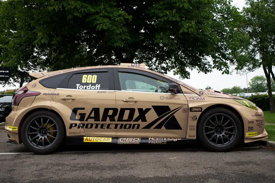 A side view of a racing car with promotional decals, parked under a green tree.