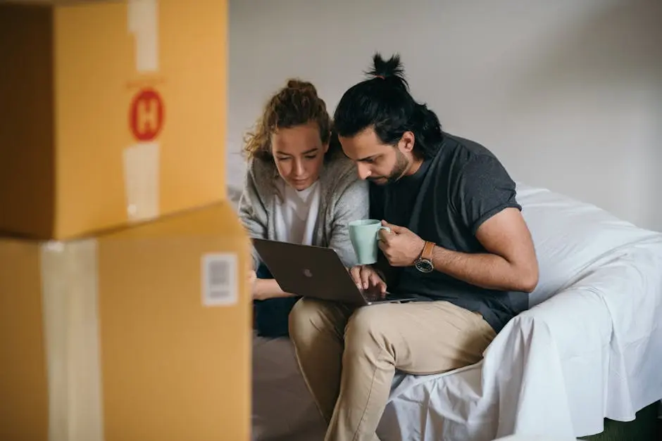 Couple surrounded by boxes checks laptop details on moving day.