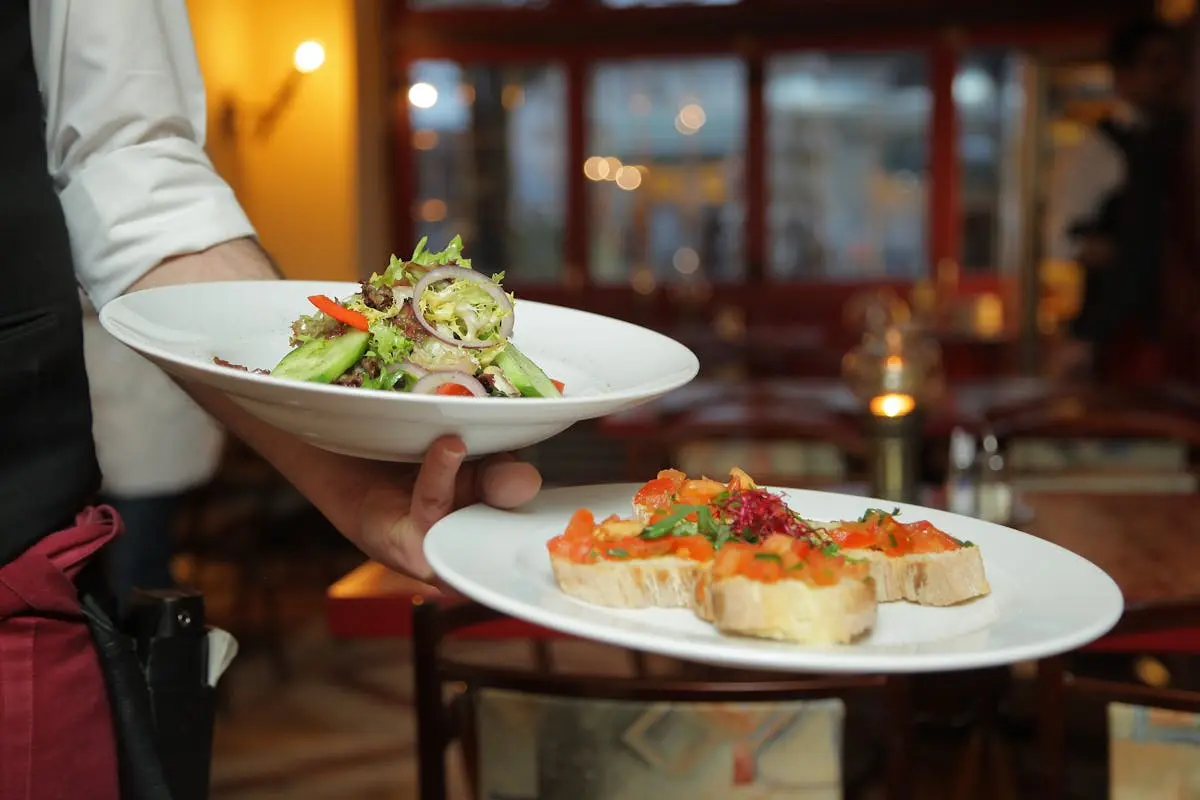 A waiter serves a fresh salad and hors d’oeuvres in a cozy restaurant setting.