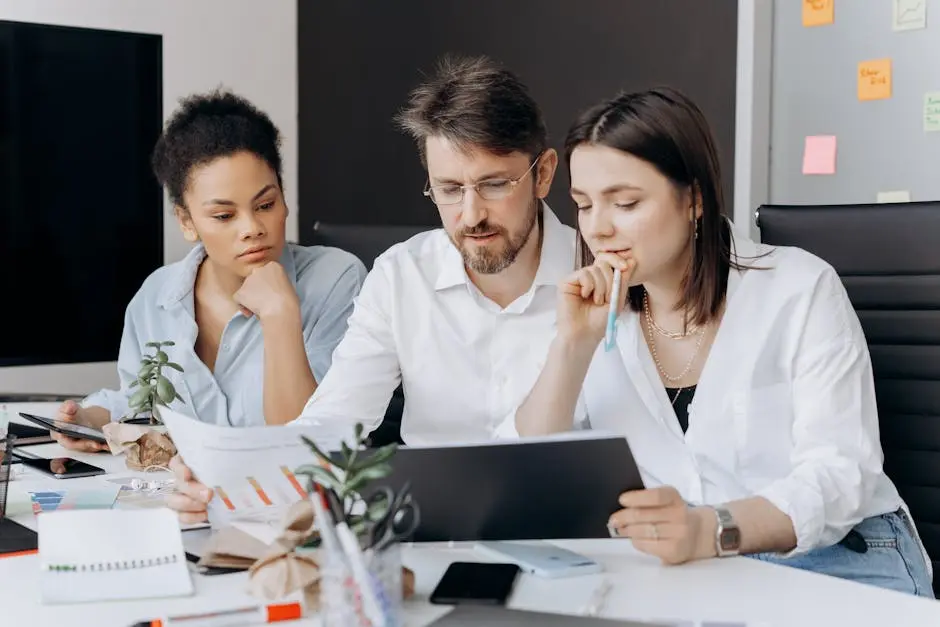 Three coworkers collaborating on a project at a modern office desk with charts and laptops.