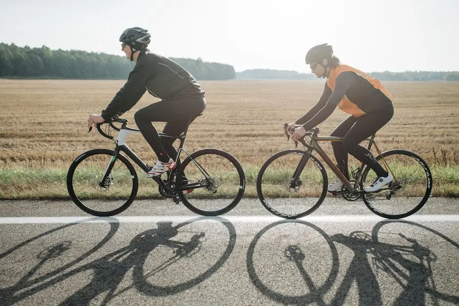Two cyclists biking on a sunny road beside harvested fields, emphasizing outdoor fitness.