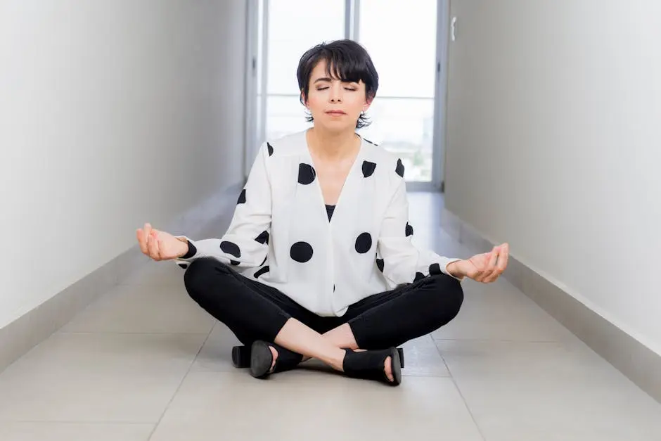 A woman practices meditation seated cross-legged in a calm and serene indoor hallway.