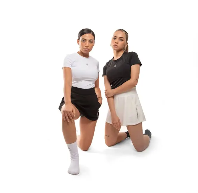 Two women in sporty attire pose in a studio, showcasing modern activewear fashion.