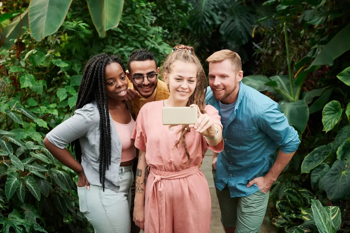 Four friends smiling and taking a selfie amidst lush greenery, capturing a joyful moment outdoors.