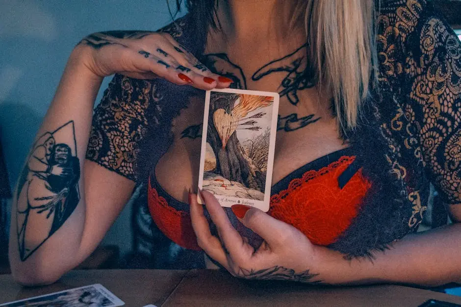 A woman in red lingerie holds a tarot card, showcasing intricate tattoos and mysterious vibes.