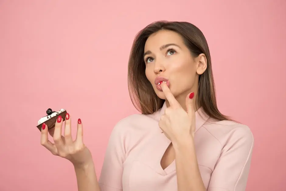 A young woman with long hair savoring a tasty cupcake, posing against a pink background.
