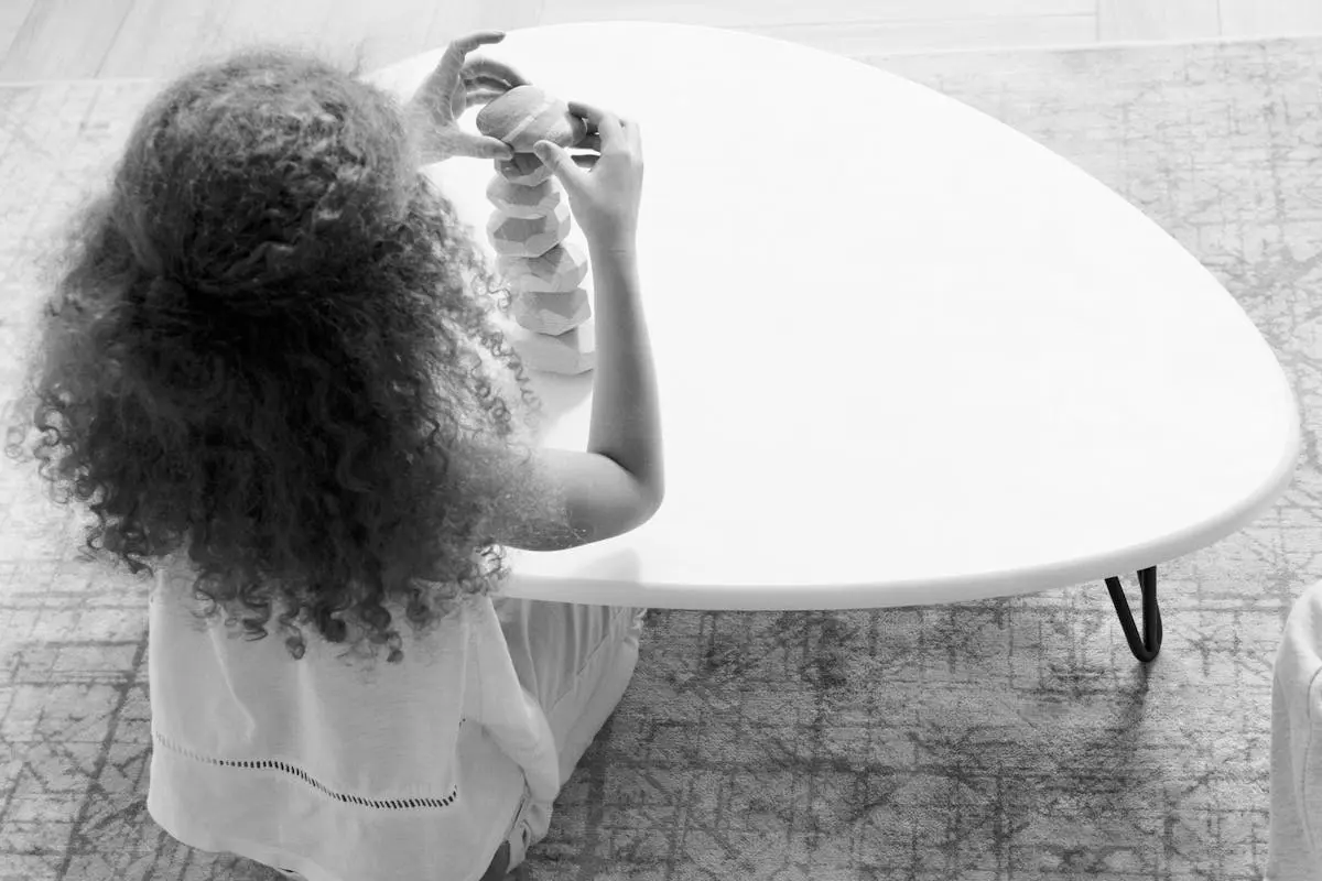 A young girl with curly hair stacking stones on a white table, promoting focus and mindfulness.