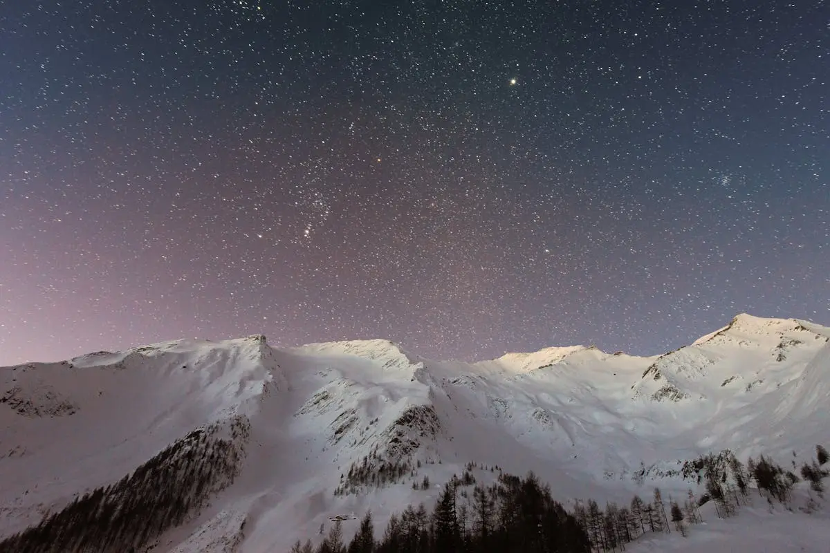 A breathtaking view of snow-capped mountains under a starry night sky, capturing the beauty of winter outdoors.