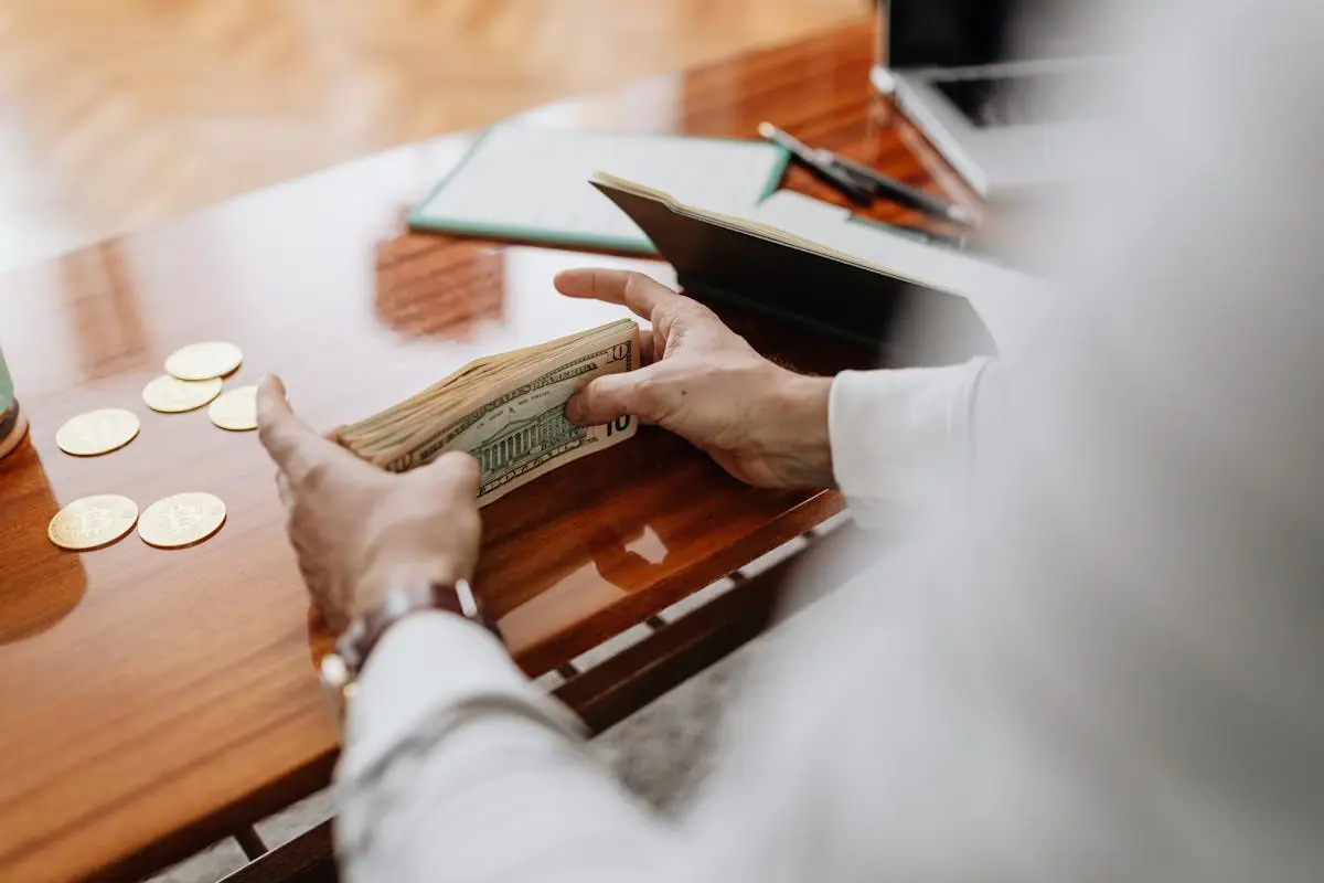 Person counting cash and coins on a wooden table, emphasizing financial tasks. cfo