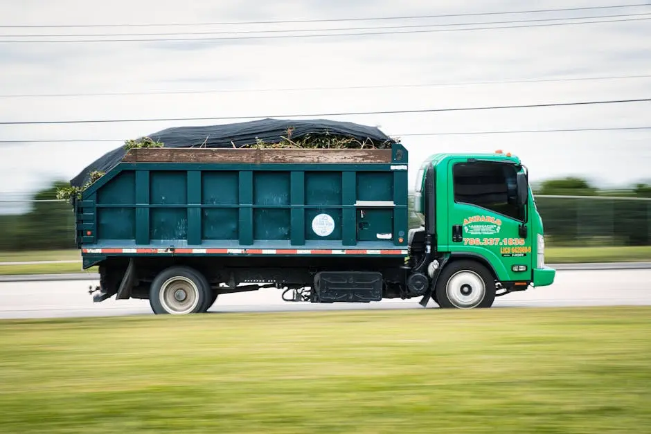 A green truck transporting yard waste on a road captured in motion. Perfect for transportation and environmental themes.